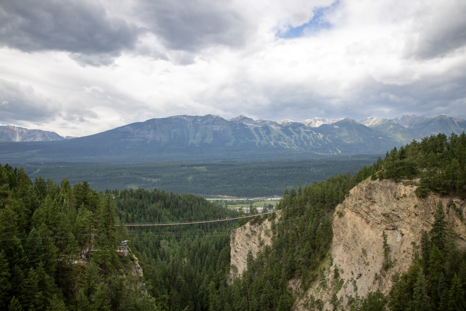 A suspension footbridge over a canyon with layered mountain ridges behind and a dramatic bank of cloud above.
